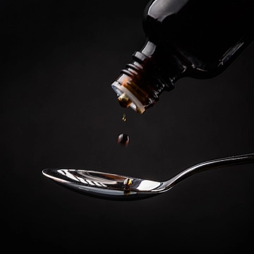 Nahaufnahme einer Tropfenflasche, die homöopathische Flüssigkeit in einen Löffel tropft
